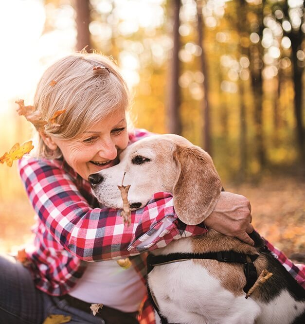 A woman hugging her dog while sitting in fallen Autumn leaves